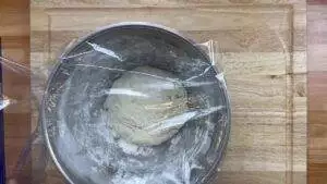 Bread dough rising in a covered bowl on a wooden surface, ready for baking.