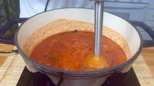 Blending homemade tomato soup in a pot, using a hand blender for a smooth, fresh texture.