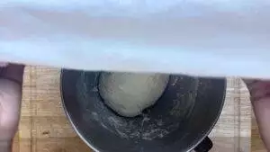 Bowl of dough covered with a white cloth on a wooden table, ready for rising. Perfect for bread-making tips.