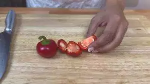Person slicing red peppers on a wooden cutting board with a knife nearby.