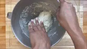 Hands kneading dough in a metal bowl on a wooden surface. Baking preparation at home.