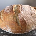 Freshly baked artisan bread loaf cooling on a wire rack with a golden crust.