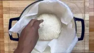 Hand preparing dough in a lined Dutch oven for bread baking.