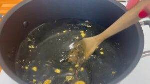 Stirring a pot of clear liquid with yellow granules using a wooden spoon, cooking on a stove.