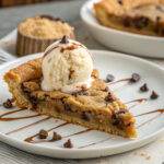 Slice of chocolate chip cookie pie topped with vanilla ice cream and caramel drizzle on a white plate.