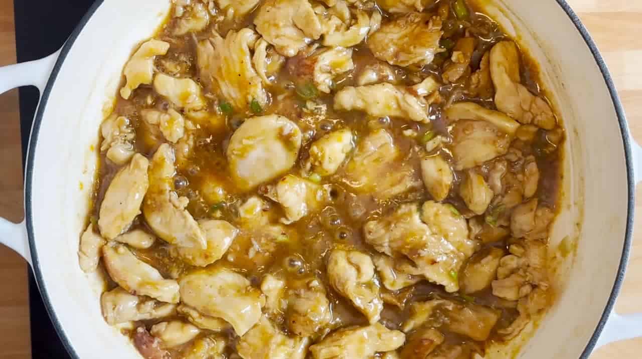 Delicious simmering chicken stew with savory sauce in a white pot on a stovetop. Perfect for a hearty meal.