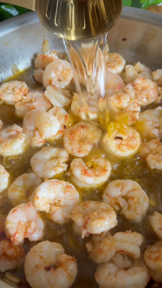 Pouring wine into a pan of cooking shrimp.