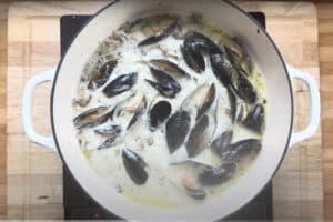 Cooking mussels in creamy white sauce in a white pot on a stovetop.