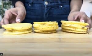 Sliced potatoes on a wooden board, ready for cooking. Close-up of hands arranging the thin potato slices.