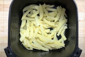 Raw potato fries in an air fryer basket ready for cooking. Perfect for a healthy homemade snack.