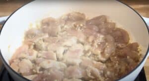 Cooking chicken pieces in a white pot on a stovetop, ready for a delicious meal preparation.