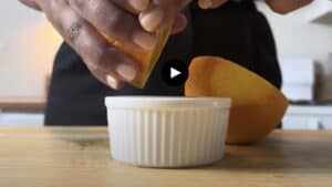 Squeezing fresh orange juice into a white ramekin on a wooden countertop in a kitchen setting.