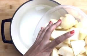 Person adding chopped potatoes into a pot of water on a wooden surface.