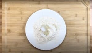 White plate with flour and spices on a wooden cutting board, ready for mixing. Ideal for cooking preparation visuals.