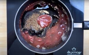 Tomato sauce and spices simmering in a pan on an induction cooktop.