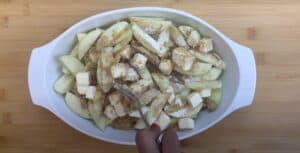 Sliced apples with butter, brown sugar, and cinnamon in a baking dish being prepared for a delicious apple dessert.