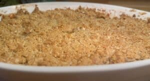 Golden apple crumble dessert in a white baking dish, with a crispy oat topping, ready to serve.