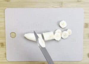 Slicing a banana on a cutting board with a knife, perfect for healthy snack preparation or recipe ingredients.