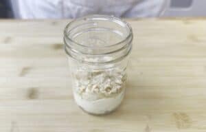 Jar of layered flour and breadcrumbs on a wooden table.