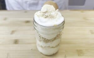 Creamy banana pudding in a mason jar topped with crushed wafers on a wooden table.