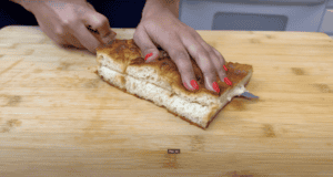 Person slicing homemade focaccia bread on a wooden cutting board.