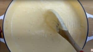 Creamy cheese sauce being stirred in a pot with a wooden spoon, perfect for pasta or dipping.