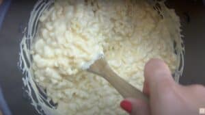 Creamy mac and cheese being stirred in a pot with a wooden spoon.