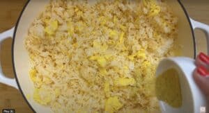 Fried rice with scrambled eggs in a pan, being seasoned with spice mix from a white bowl.