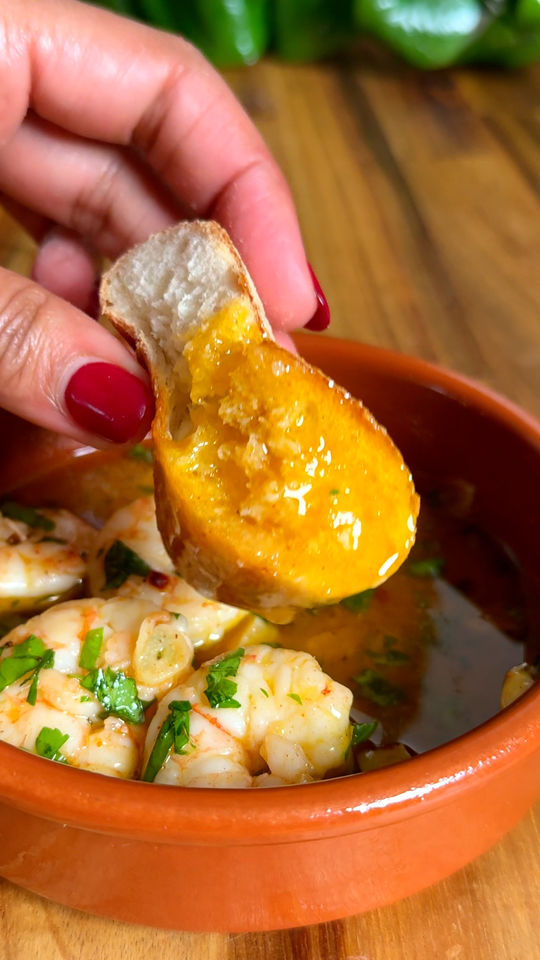 Hand dipping bread into garlic shrimp in an orange bowl.