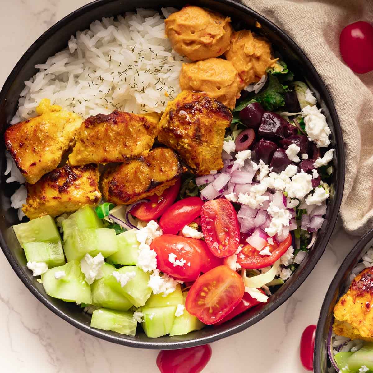Chicken Mediterranean Bowl with grilled chicken, rice, hummus, cucumber, tomato, onion, feta cheese, beets on a marble surface.