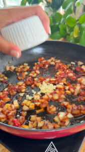Adding garlic to sautéed onions in skillet.