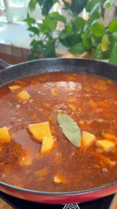 Diced potatoes and a bay leaf in tomato sauce in a pot.