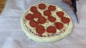 Homemade pepperoni pizza on parchment paper, ready to bake with scissors nearby. Perfect for pizza lovers!