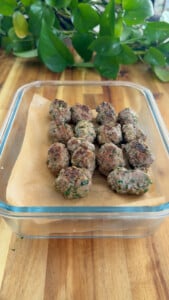 Homemade meatballs in a glass container on a wooden table with green plant in the background.