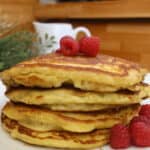 Stack of homemade pancakes topped with fresh raspberries on a white plate.