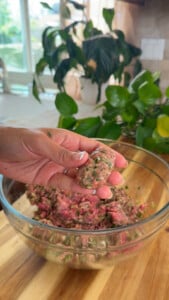 Hand shaping meat mixture in glass bowl for cooking with fresh herbs.