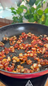 Sizzling diced onion in a black skillet with green plants in the background.
