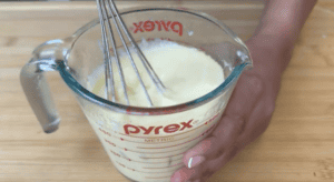 Whisking creamy batter in a Pyrex measuring cup on a wooden surface.