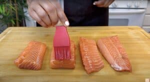 Brushing oil on fresh salmon fillets on a wooden board, preparing for cooking.