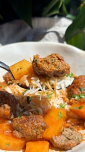 Close-up of a forkful of spiced meatballs, tender potato, and fluffy rice against a sunny background.