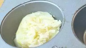 Muffin tin with potato slices topped with grated cheese, ready for baking.