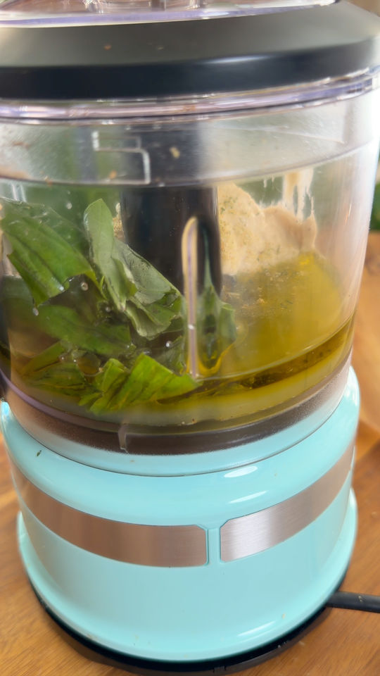 Food processor with basil, oil, and other ingredients inside.