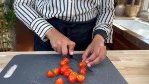 Person chopping cherry tomatoes on a cutting board in a kitchen.