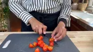 Person chopping cherry tomatoes on a cutting board in a kitchen.