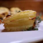 Golden potato stacks garnished with herbs on a white plate.