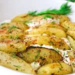 Delicious oven-roasted potatoes with herbs and spices, garnished with fresh dill in a white dish.