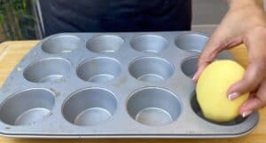 Hand placing potato into muffin tin cavity for creative cooking.