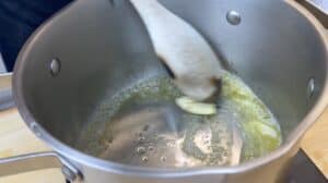Stirring melting butter and garlic in a stainless steel pot with a wooden spoon for a cooking preparation.