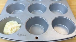Empty muffin pan with batter and cheese in one cup, ready for baking.