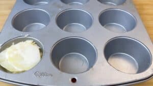 Muffin tin with sliced potatoes and cheese in one cup, ready for baking.